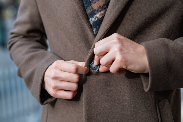 Un uomo d'affari chiude un bottone sul cappotto in primo piano - Foto, immagini