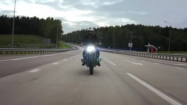 Человек едет скремблер мотоцикл по шоссе через лес, вид спереди - Кадры, видео
