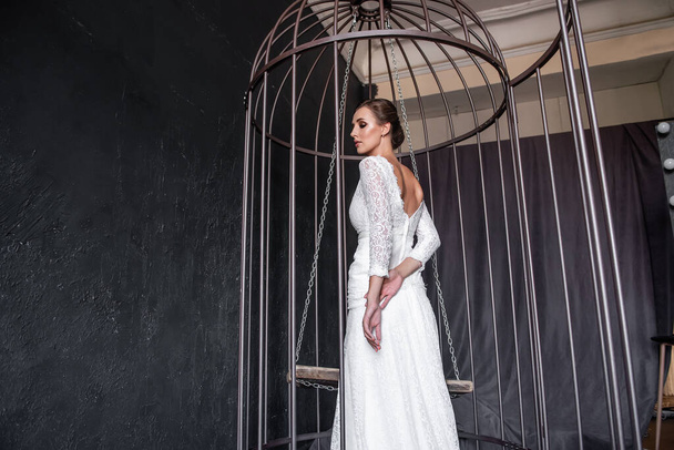 Fashion bride in an iron cage, unhappily looking out from behind bars. Life out of will. A fictitious marriage of convenience. Break out of your comfort zone. Patriarchal marriage concept. Copy space - 写真・画像