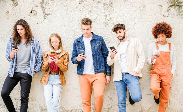 Multicultural group of friends using cellphones outdoors - Students browsing internet holding mobile smarphones standing beside wall - Фото, изображение