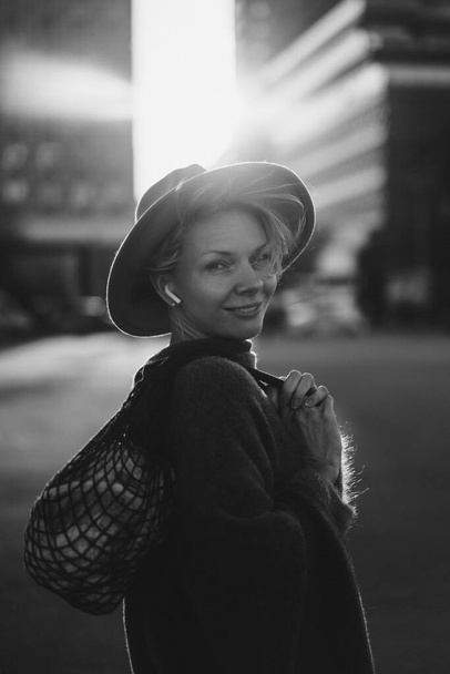 Beautiful middle-aged woman in a hat with a short haircut in the center of a big city. Close-up portrait, soft backlight. - Photo, Image