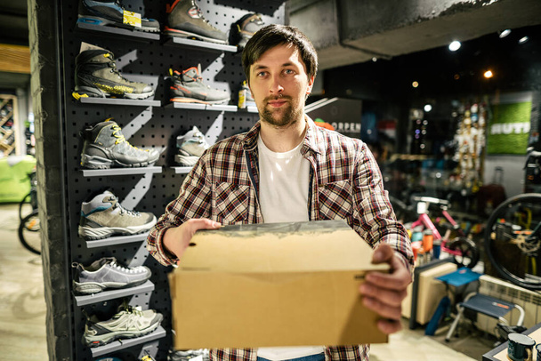 Caucasian male salesman consultant in outdoor store presenting hiking boots to buyer. A salesperson at a sports store helps a shopper to choose hiking boots. Seller in sporting goods store. - Photo, Image