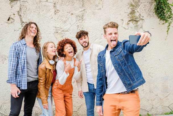 Szczęśliwi młodzi ludzie robiący selfie w mieście - Wielorasowa grupa przyjaciół robi zdjęcie patrząc w kamerę - Zdjęcie, obraz