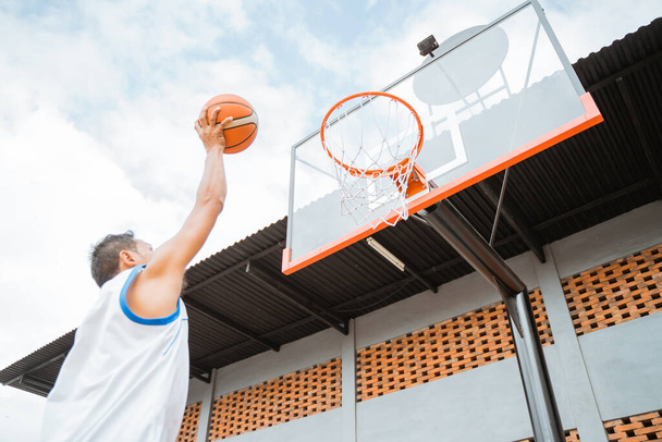 Ein Basketballspieler, der einen Ball in der Hand hält, schießt in den Korb - Foto, Bild