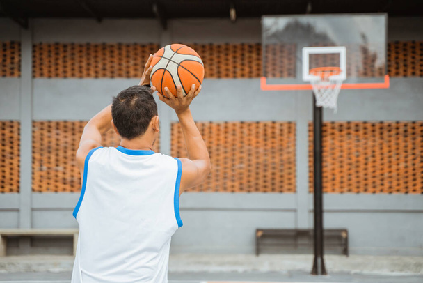 back view of a basketball player holding the ball while jump shot into the hoop - Foto, Imagem