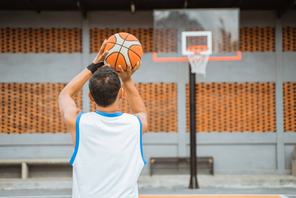 back view of a male basketball player holding the ball while shooting at the hoop - Fotó, kép