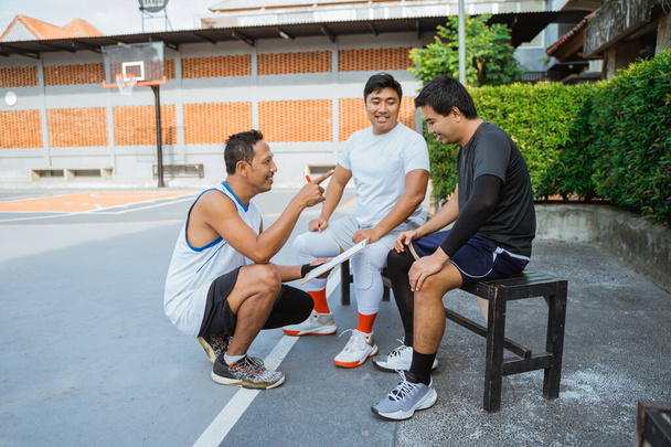 coach holding a clipboard giving instructions to two basketball players - Фото, изображение