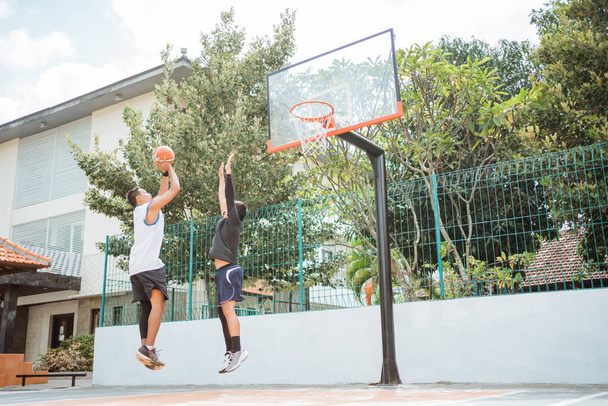 een mannelijke basketbalspeler neemt een sprong schot en wordt geblokkeerd door zijn tegenstander met beide handen - Foto, afbeelding