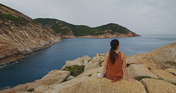 Nainen istuu kivellä ja katsoo merta.
 - Valokuva, kuva