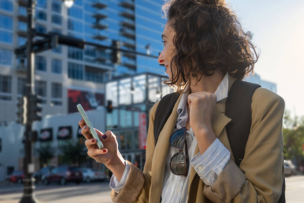 Ritratto di donna con giacca, zaino e cellulare in mano in città, concetto nuovi inizi, con spazio per copiare. - Foto, immagini