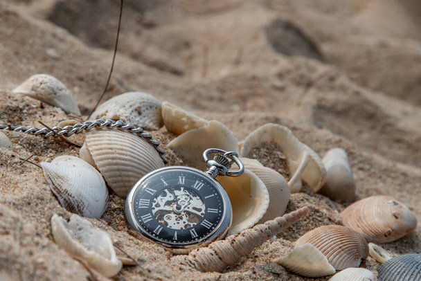 Antique pocket watch and shells in sand on the beach and copy space. Time of life in nature concept. Selective focus. - Valokuva, kuva