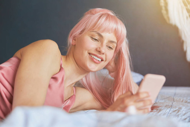 Mujer joven con pelo brillante mira a la pantalla del teléfono móvil en la cama - Foto, Imagen