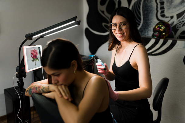 彼女のスタジオでタトゥーを入れながらカメラを見て笑っている興奮した女性アーティストの肖像画 - 写真・画像