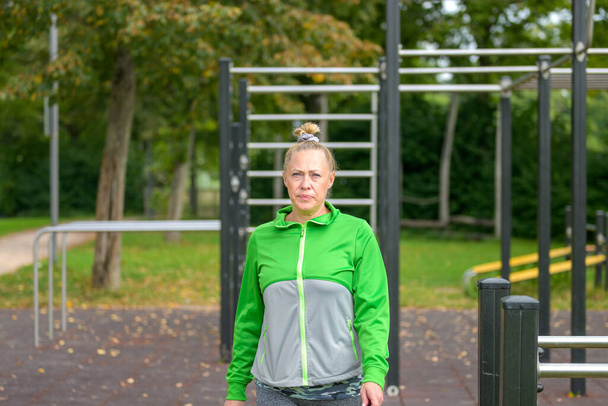 Athletic middle-aged woman looking pensively at the camera with a frown as she pauses during her workout on outdoor sporting equipment in a park - Φωτογραφία, εικόνα