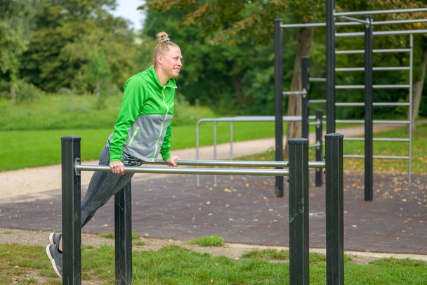 Femme sportive dans la quarantaine travaillant sur des barres parallèles dans un espace sportif extérieur dans un parc de printemps dans un concept de santé et de remise en forme - Photo, image