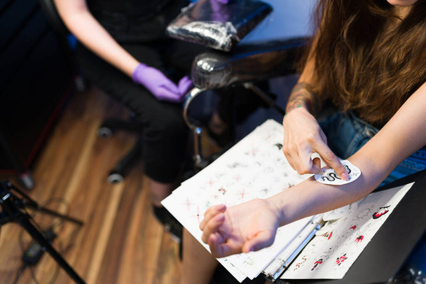 Ich lasse mir dieses Tattoo stechen. Hochwinkel einer jungen Frau, die sich im Tätowierladen eine Schablone auf den Arm legt - Foto, Bild