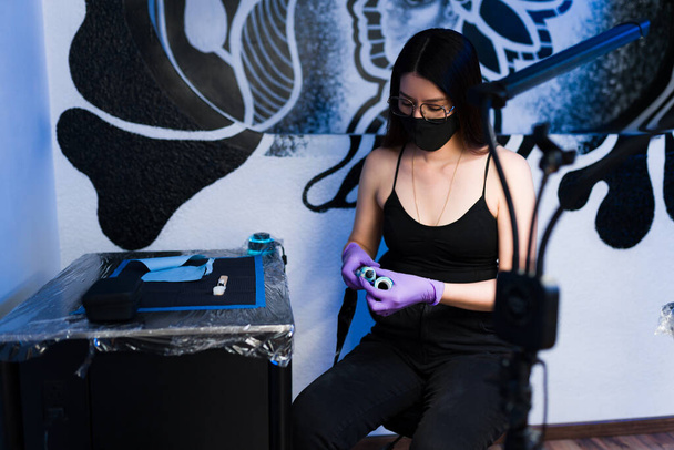 Schöne junge Frau mit Gesichtsmaske beim Vorbereiten der Tinte im Tätowierstudio - Foto, Bild