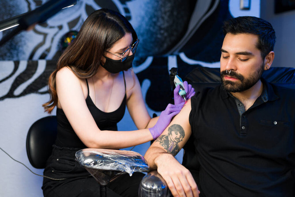 Schöne professionelle Künstlerin macht ein neues Tattoo auf dem Arm eines hübschen jungen Mannes - Foto, Bild