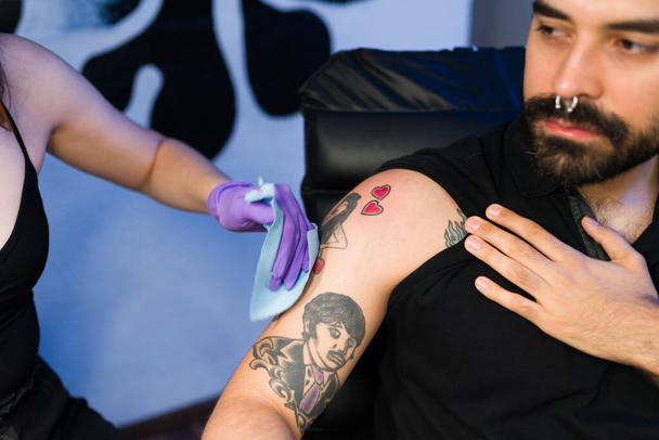 Detailní záběr rukou profesionálního umělce s ochrannými rukavicemi čistí oblast kůže po tetování - Fotografie, Obrázek