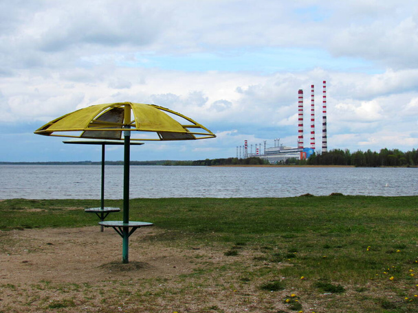 Central hidroeléctrica y playa abandonada con sombrillas rotas en el lago. El concepto de calentamiento global y cambio climático debido a las emisiones de gases de efecto invernadero. - Foto, Imagen