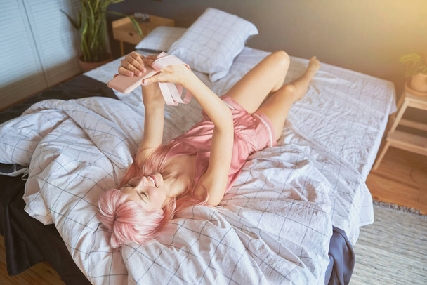 Красива щаслива леді в елегантному шовковому одязі бере селфі лежить на великому ліжку
 - Фото, зображення