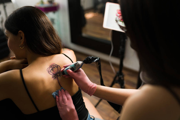 Закрыть новую татуировку спины привлекательной латинской женщины. Молодая женщина использует татуировочный аппарат в студии - Фото, изображение
