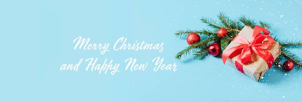 Boîte festive avec un arc rouge gros plan sur un fond bleu avec des boules de jouets de Noël une branche d'épinette moelleuse scintille et confettis. Nouvel An Noël concept.  - Photo, image