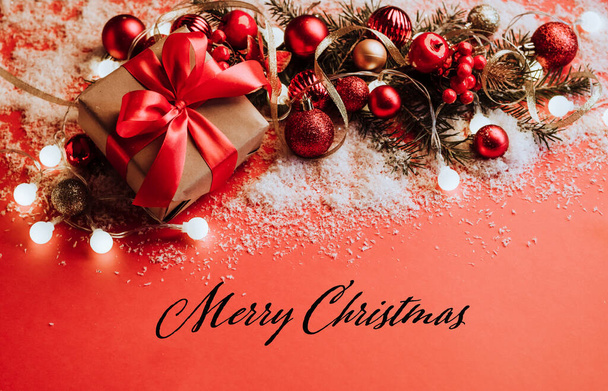 Karácsonyi ajándékok piros és arany karácsonyi labdák koszorú bolyhos fenyő ágak piros háttér hópelyhek, csillogás, konfetti. Ünnepi karácsonyi kártya sablon kifejezéssel Boldog Karácsonyt - Fotó, kép