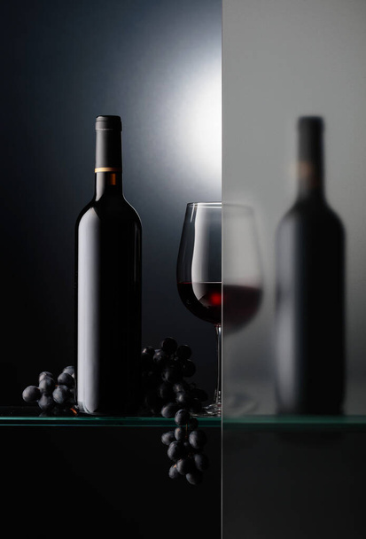 Flaschen und ein Glas Rotwein mit einem Bund blauer Trauben. Das Stillleben ist teilweise mit einem Milchglas überzogen. - Foto, Bild