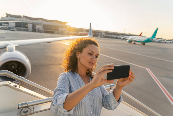 Çekici yetişkin kadın uçakla uçmadan önce selfie çekiyor. - Fotoğraf, Görsel