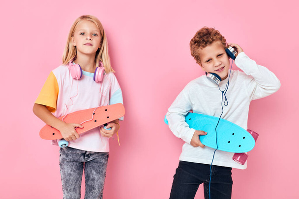 милый мальчик и девочка держат скейтборды развлекательные наушники музыка - Фото, изображение