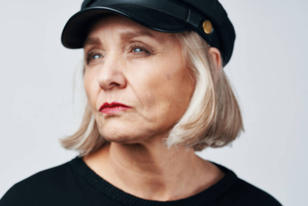 oudere vrouw in een zwart hoed mode close-up licht achtergrond - Foto, afbeelding