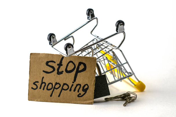 il concetto di rifiuto di acquistare un consumo ragionevole è un carrello rovesciato con un lucchetto x chiavi e un segno con l'iscrizione stop shopping. Foto di alta qualità - Foto, immagini