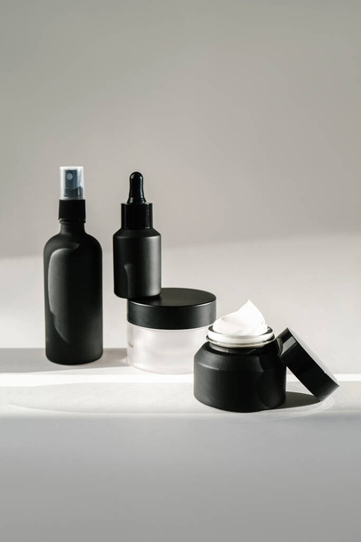 Vier zwarte cosmetische flessen op een achtergrond overspoeld met zonlicht. - Foto, afbeelding