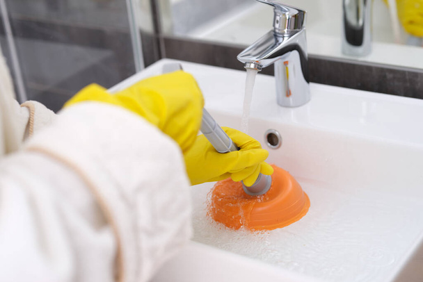 A sárga kesztyűs személy a mosdókagylót takarítja az elzáródás közeléből. - Fotó, kép
