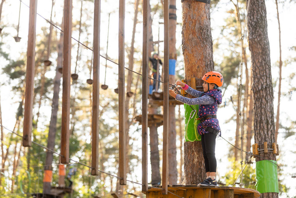 Meisje klimmen in adventure park is een plaats die kan bevatten een grote verscheidenheid van elementen, zoals touwklimmen oefeningen, hindernisbanen en zip-lijnen. - Foto, afbeelding