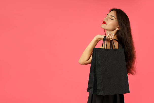 Attractive girl in black dress with paper bags on pink background. - Photo, Image