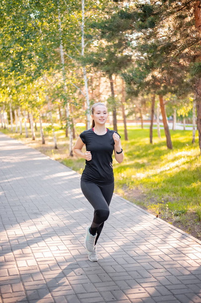 A girl in a black sports uniform is jogging in the evening park. Self-sports concept. - Foto, Imagem