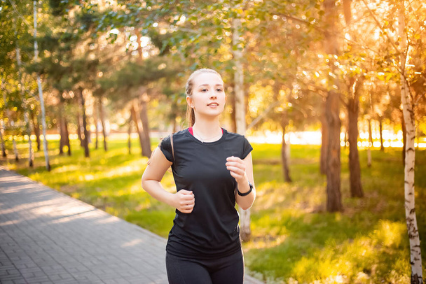A girl in a black sports uniform is jogging in the evening park. Self-sports concept. - Foto, afbeelding