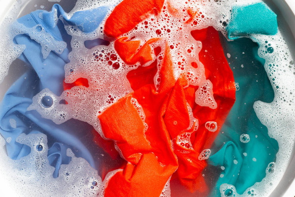 Χρωματιστά ρούχα μουλιάζουν σε σκόνη διάλυση απορρυπαντικού νερού. Έννοια πλυντηρίου - Φωτογραφία, εικόνα