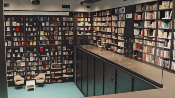 Geen mensen dolying-in slow mo shot van teller en vele kleurrijke boeken in boekenkasten in de moderne bibliotheek - Video