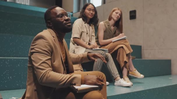 Közepes lassítású felvétel fiatal felnőtt afro-amerikai férfi egyetemi hallgató felemelt kezét során érdekes előadás megosztani véleményét a témában, nevetve együtt női osztálytársak - Felvétel, videó
