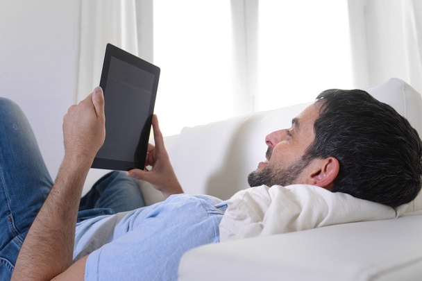 Giovane felice uomo attraente utilizzando pad digitale o tablet seduto sul divano
 - Foto, immagini