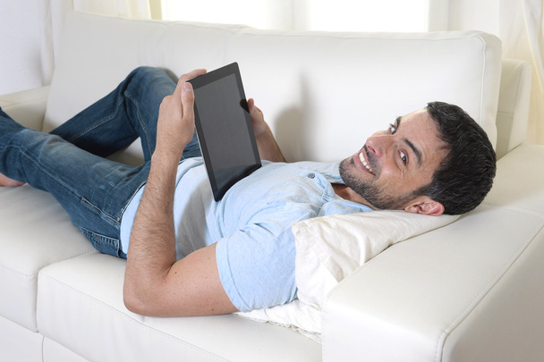 ευτυχής ελκυστική νεαρός χρησιμοποιώντας ψηφιακή μαξιλάρι ή δισκίο που κάθεται στον καναπέ - Φωτογραφία, εικόνα