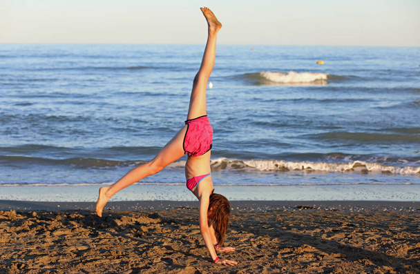 Genç atletik kız sahilde bacaklarıyla ritmik jimnastik yapıyor. - Fotoğraf, Görsel