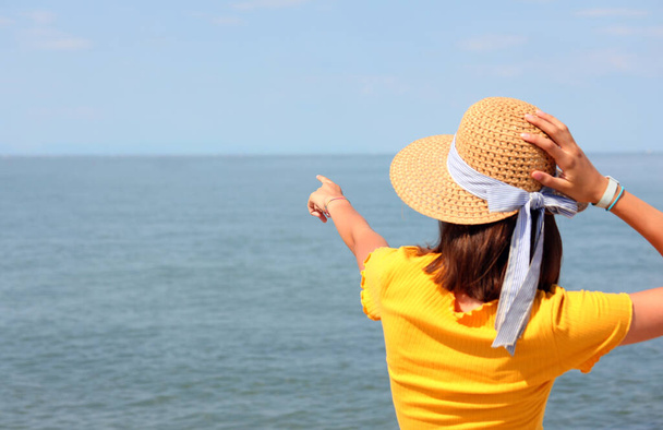 junges Mädchen mit Strohhut, das auf einen Bodenpunkt am Horizont auf dem offenen Meer zeigt - Foto, Bild