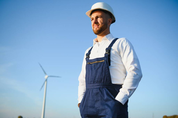 Engineer is checking energy production on wind turbine. Worker in windmills park in helmet. - Photo, image