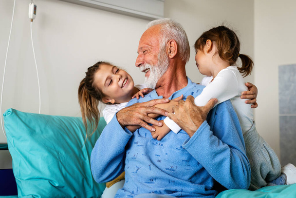 Happy recovering grandfather is visited by his grandchildren in the hospital. Healthcare, family, support concept - Фото, изображение