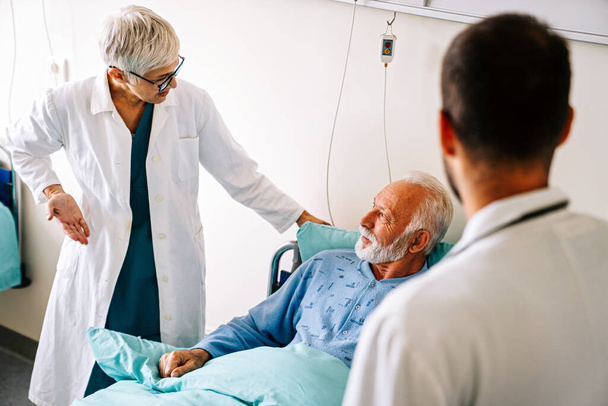 Doctor talking to senior male patient in hospital bed who is recovering from the disease. Healthcare, coronavirus, people concept. - Foto, Imagem