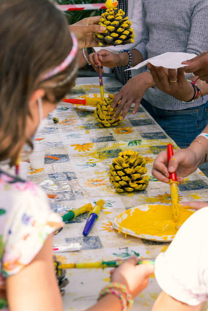 bambini che decorano pigne con vernice gialla in un laboratorio creativo di arti e mestieri - Foto, immagini